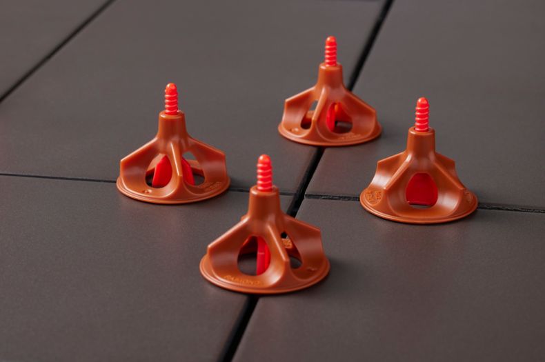 Four orange tile leveling caps on charcoal colored tiles. 