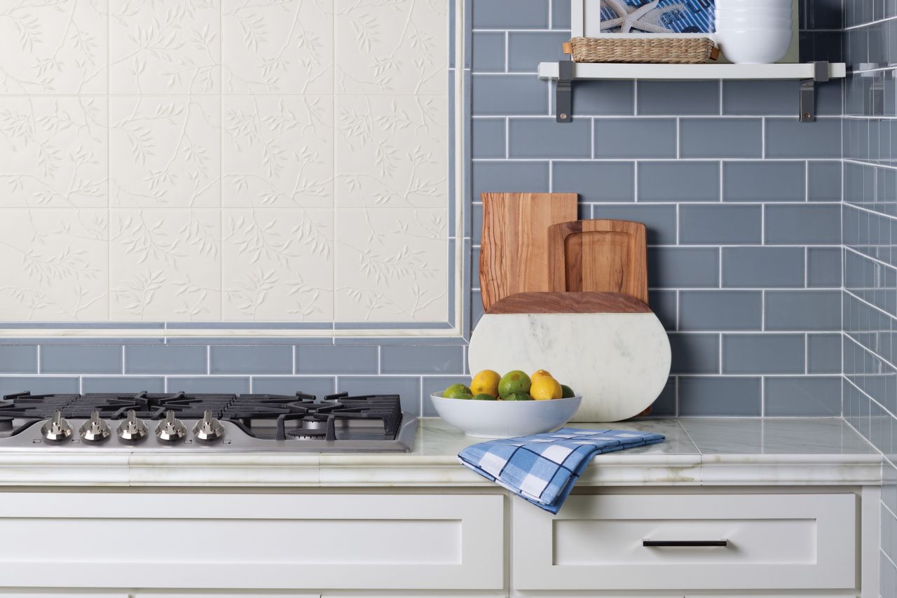Marble counter top with blue ceramic tile backsplash with framed accent tile above range top.