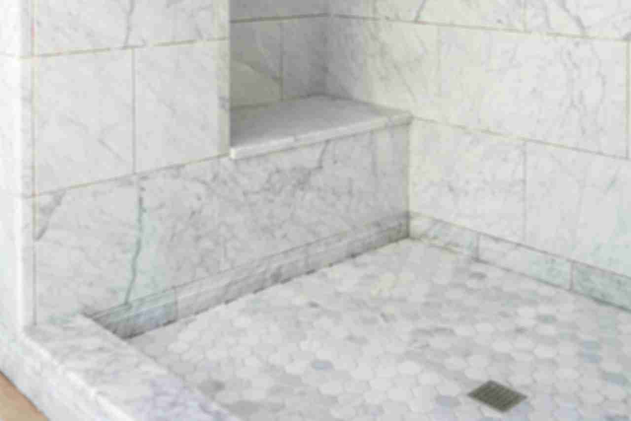 Large walk in shower tiled with grey marble and a recessed bench.
