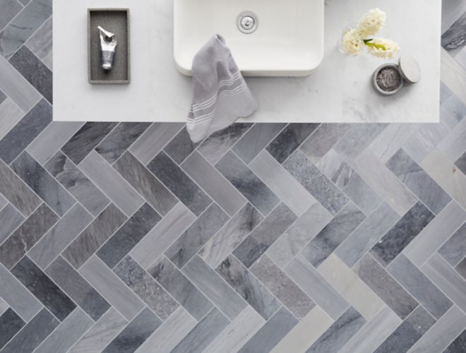 Overhead view of bathroom sink and floor featuring dramatic grey marble tile in a herringbone pattern.
