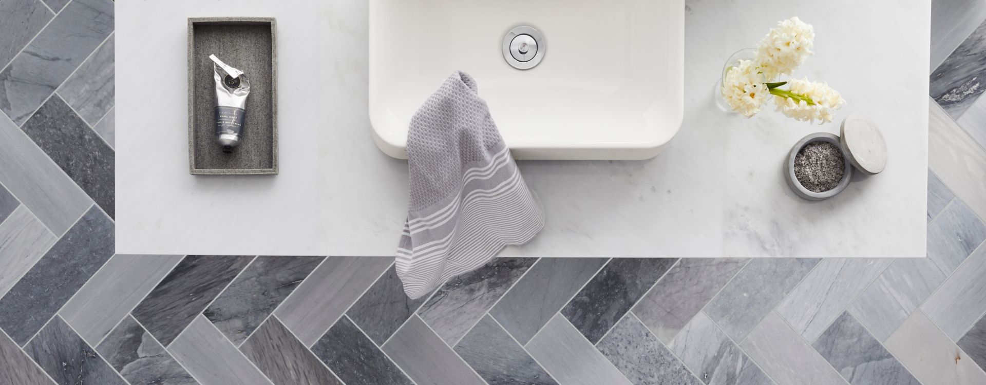 Overhead view of bathroom sink and floor featuring dramatic grey marble tile in a herringbone pattern.