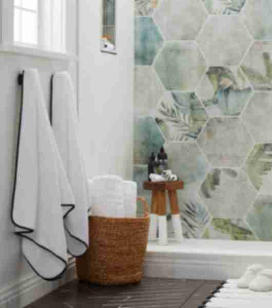 Hexagonal porcelain tile with green tones and floral print on wall. Black tile on floor. white walls of tile.
