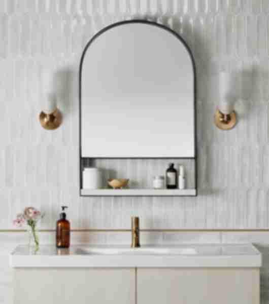 Bathroom sink vanity with soap and flowers. Mirror and white sconces on a white tile wall