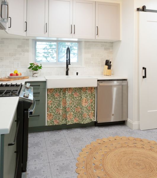 Kitchen with sink, stove and dishwasher. Green lower cabinets, white upper cabinets and colorful skirt below the sink.