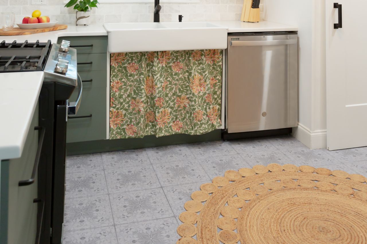 Kitchen with sink, stove and dishwasher. Green lower cabinets, white upper cabinets and colorful skirt below the sink.