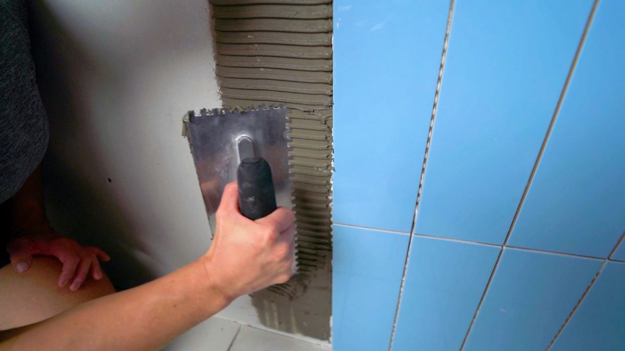 Applying thinset mortar to a wall using a notched trowel. The notches run in the same direction as the shortest edges of the tile.
