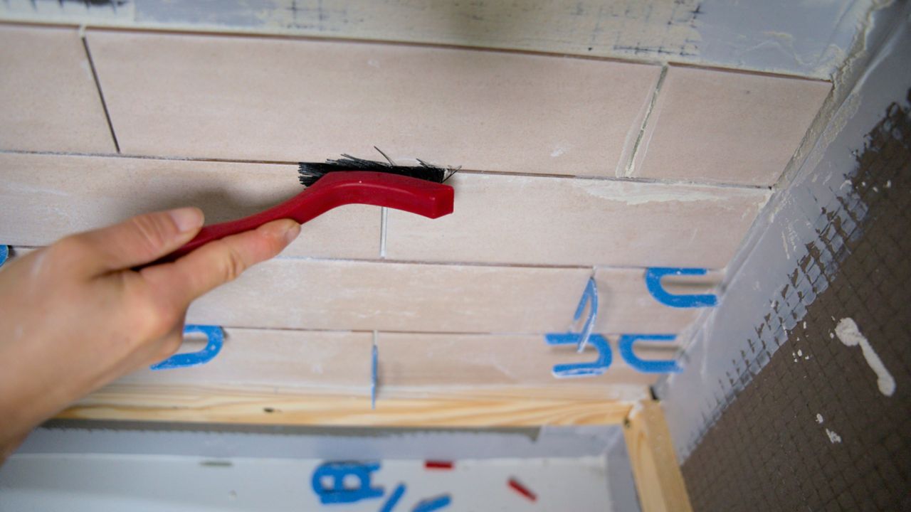 A tile pro uses a grout brush to remove traces of dried thinset from within grout joints.