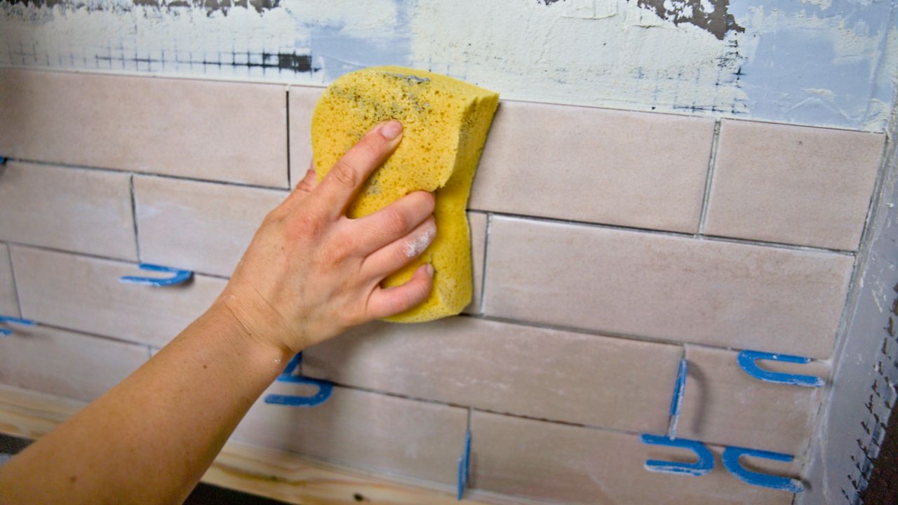 Using a soft sponge to clean traces of thinset from newly installed tiles.
