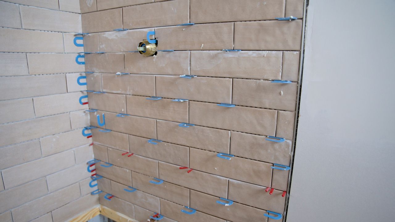 After installing shower wall tile and allowing the thinset mortar to cure, a tile pro cleans all surfaces before moving on to the grouting phase of the installation.