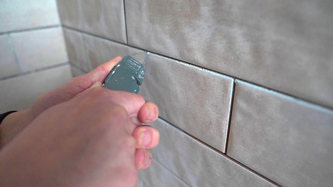 A tile pro uses a utility knife to remove stubborn thinset from grout joints.