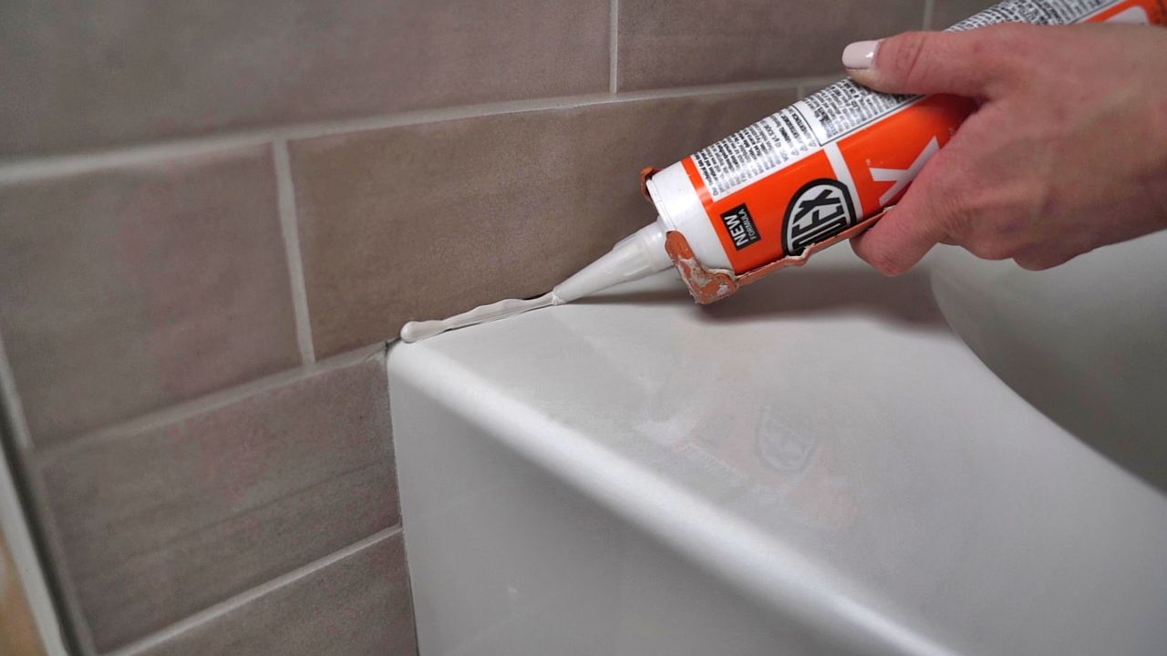 Applying silicone sealant where the tiled walls above a shower meets the edge of the tub below.