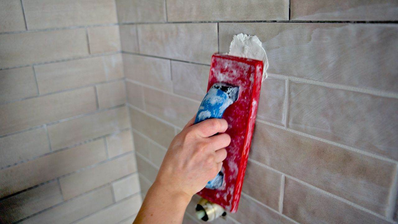 Using the short side of a grout float to apply grout to shower wall tile.