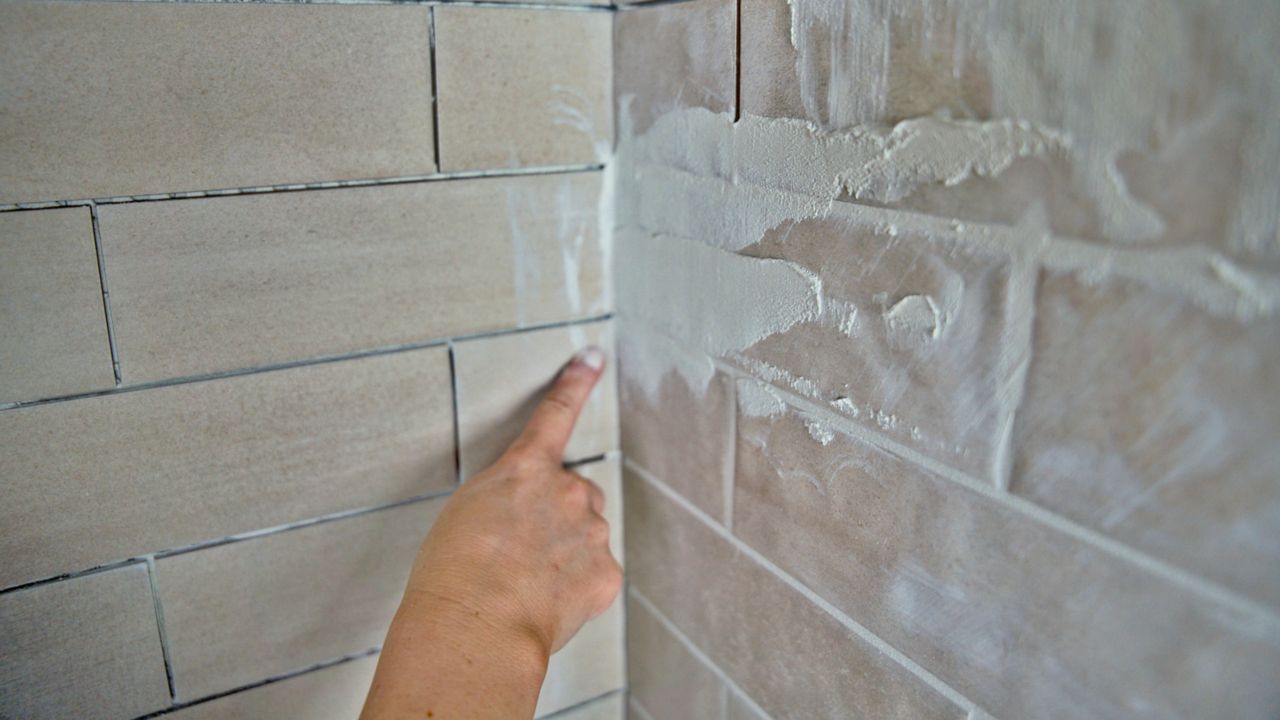 A tile pro points at an interior corner grout joint in a shower, which will need to be free of grout in order to properly fill with silicone later.