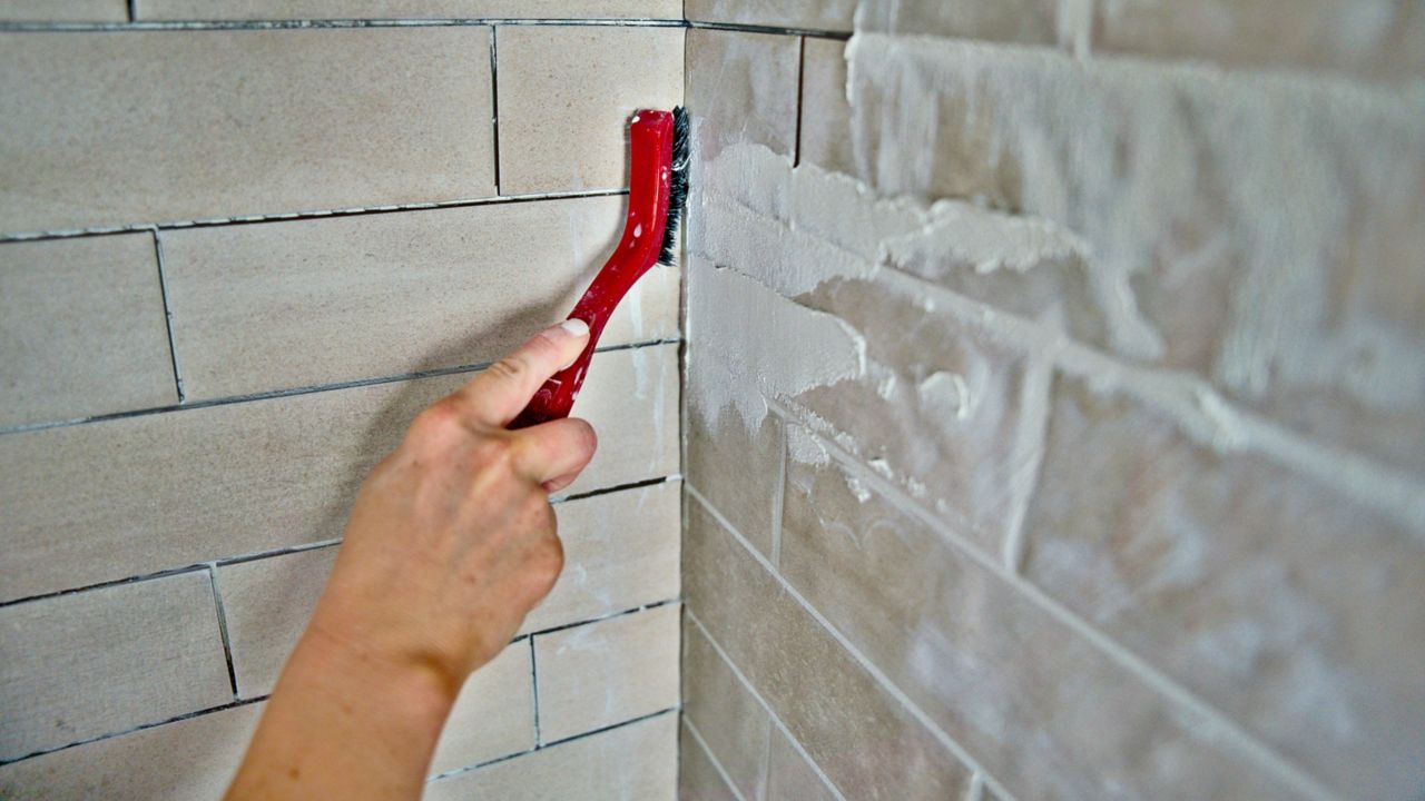 Using a grout brush to remove excess grout from inside corners before it cures.