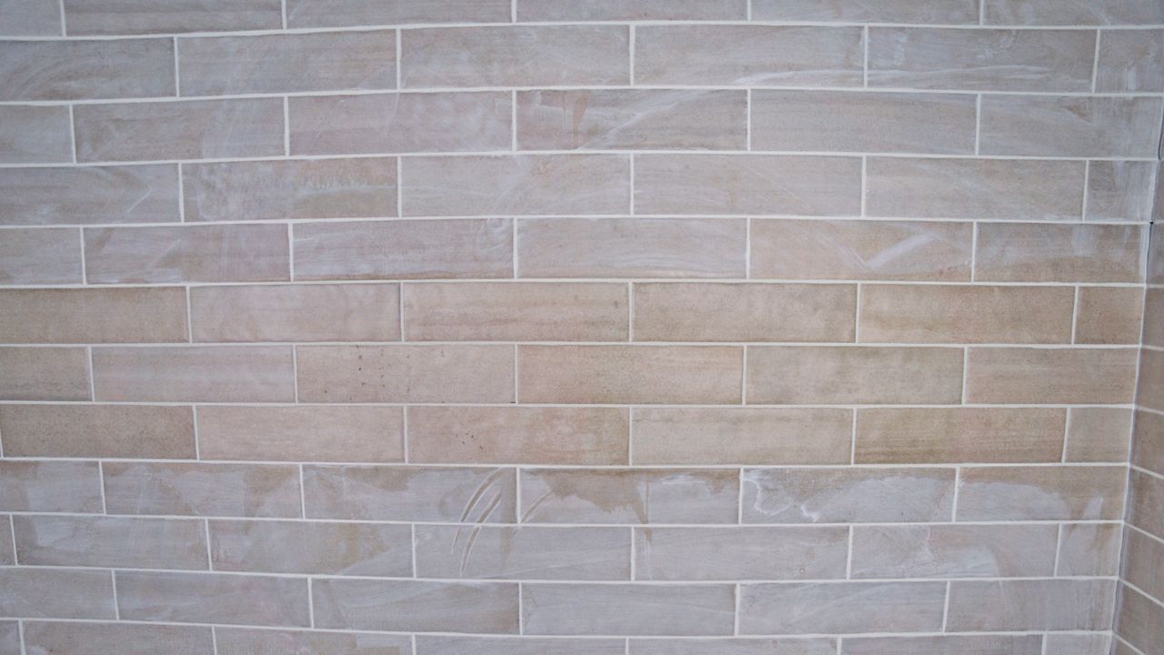 A tile pro uses a damp sponge to perform the initial cleaning of a wall of tile in a newly grouted shower.