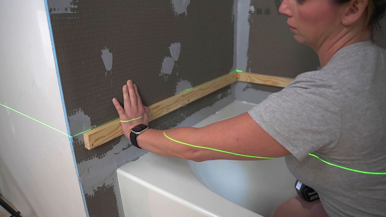 Installing a ledger board near the base of a shower wall, in order to guide the installation of the first few rows of tile.