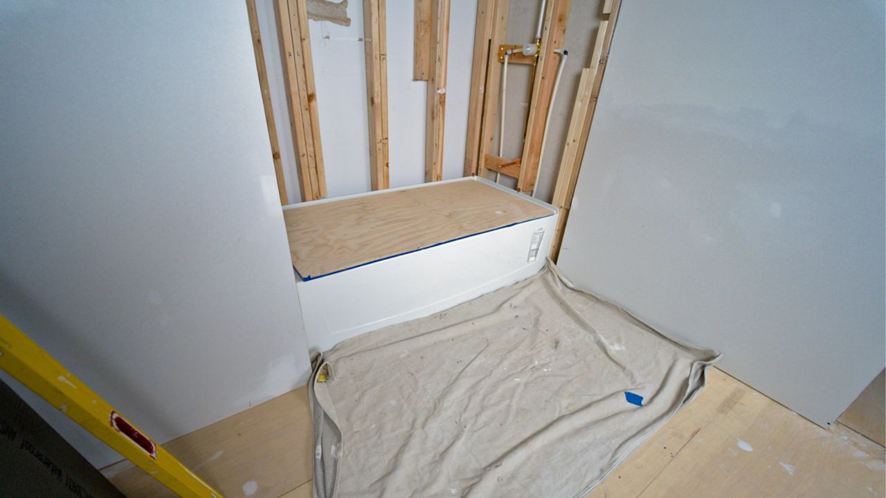  In preparation for tiling a shower, the walls above a tub have been demolished and the work area is protected with a tarp and plywood.