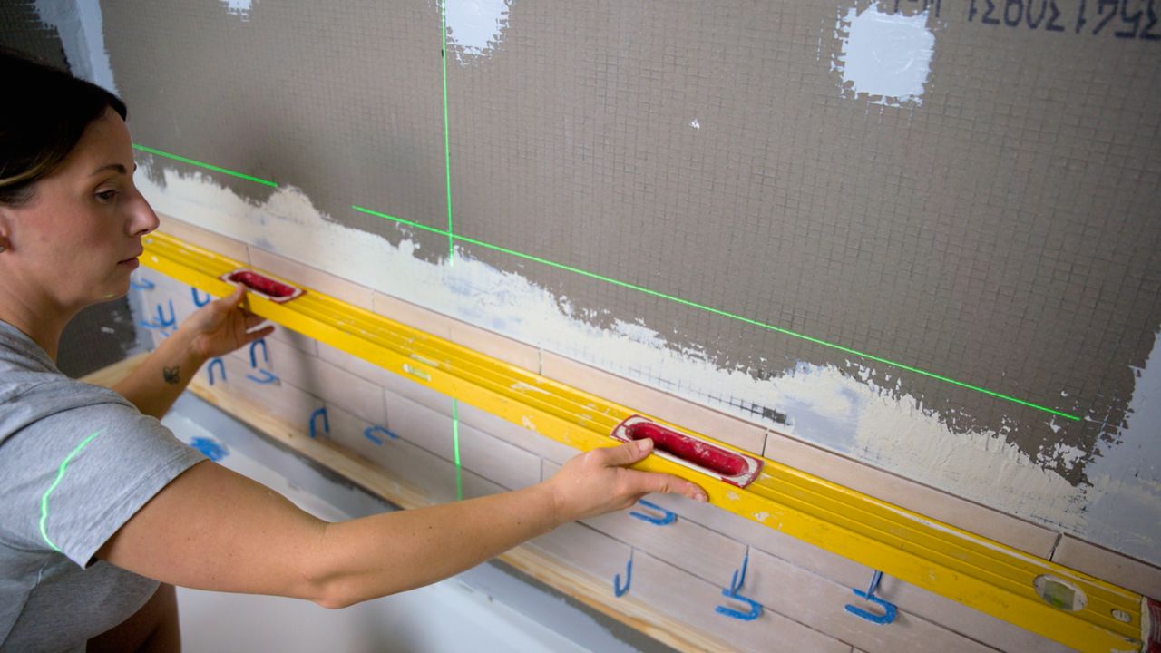 After installing several rows of shower tile, a tile pro uses her leveler tool to check that the surface of tiles are flat and free of lippage.