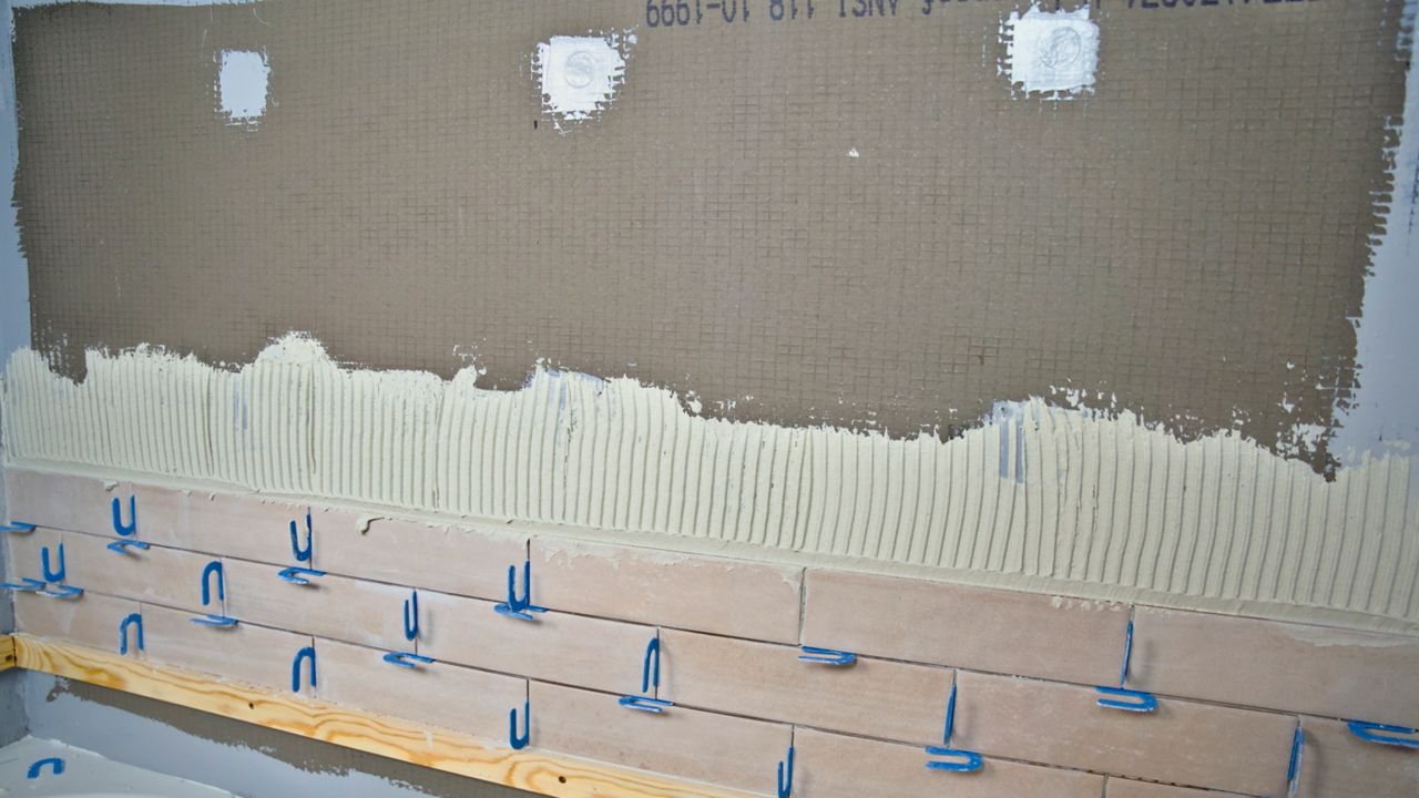 After checking that the first few rows of shower wall tile are level, a tile pro has placed spacers in the vertical and horizontal joints before proceeding.