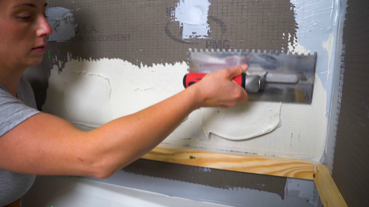 A tile pro applies the initial layer of thinset to a shower wall before installing the first row of tile.