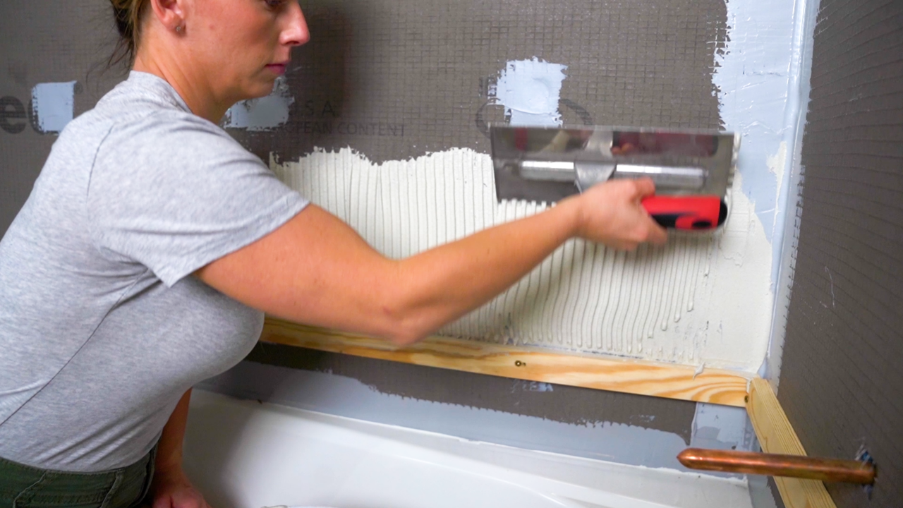 A tile pro uses the notched side of a trowel to form rows of notches into thinset, ensuring the lines run parallel to the shortest side of the tiles.