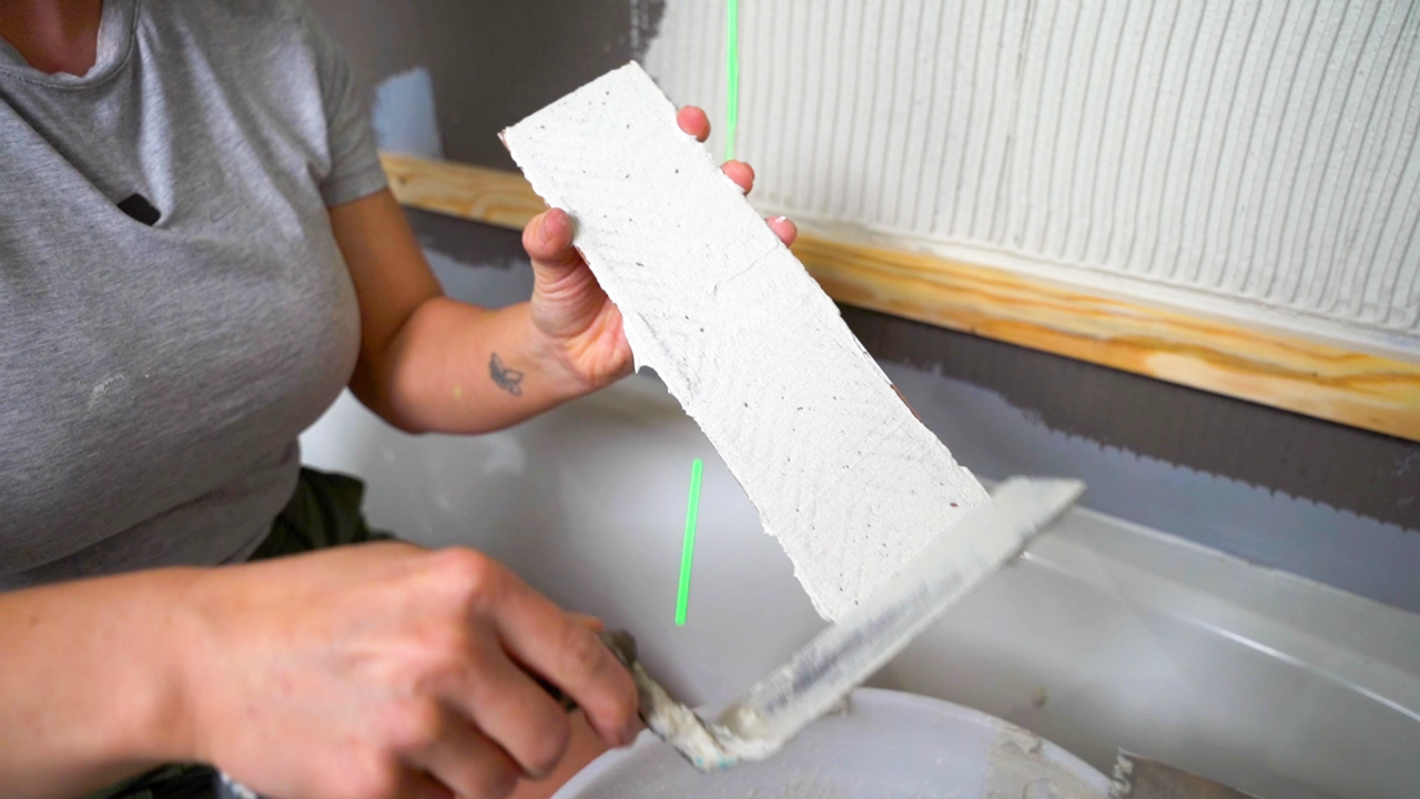 A tile pro uses a trowel to spread a small amount of thinset from edge to edge on the back side of a tile.