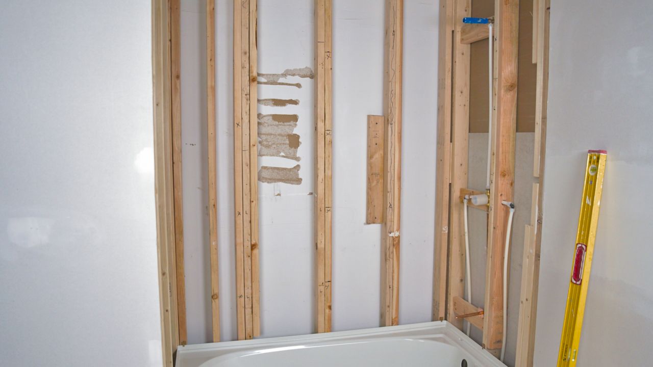 Image shows bare wall studs over a bathtub, in preparation for tiling a shower.