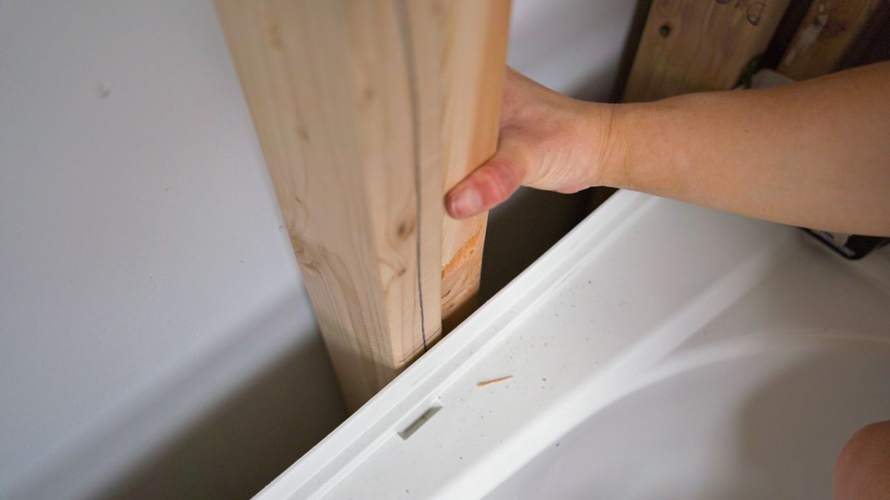 Checking the alignment of wall studs around a tub flange to ensure a level surface before tiling.