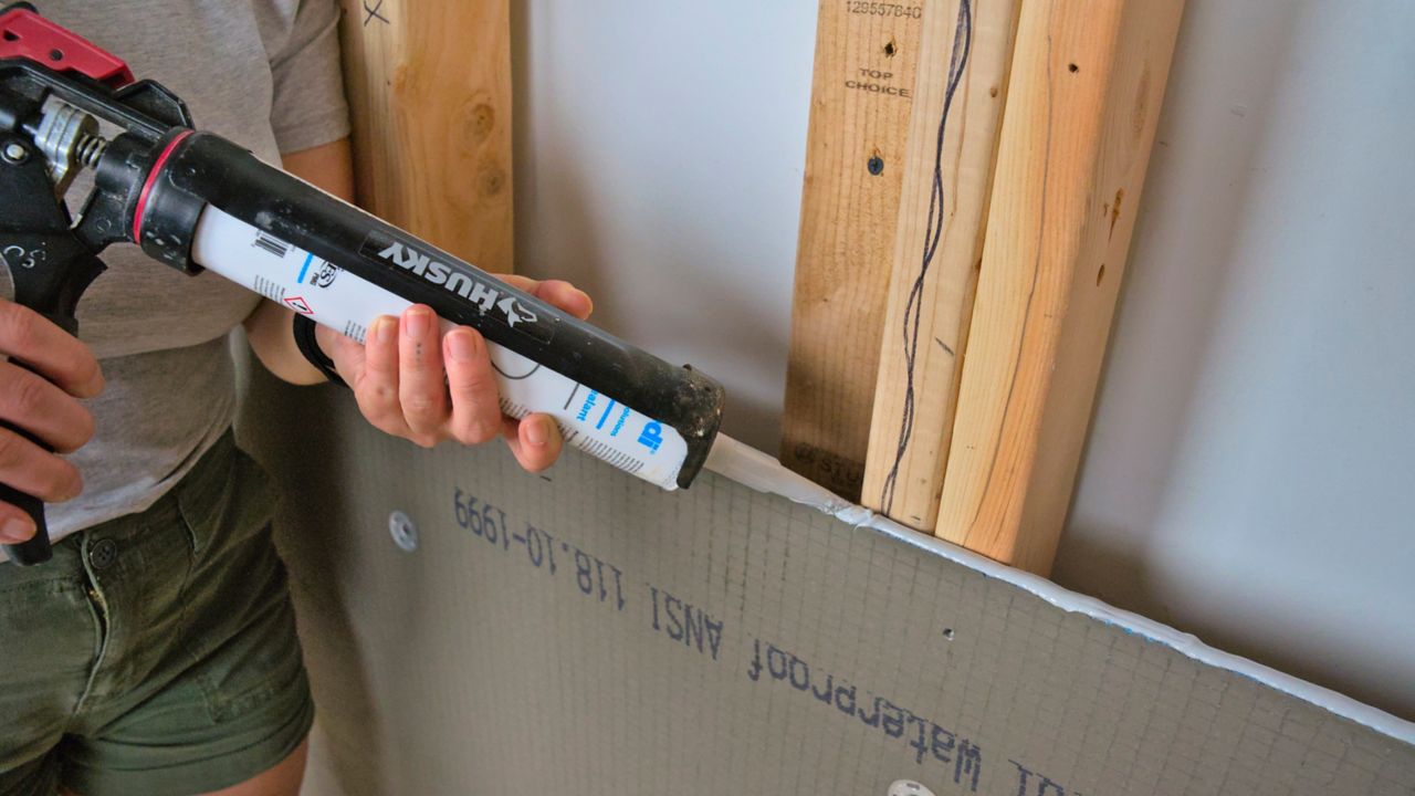 Adding waterproof sealant between board seams while installing shower wall panels.