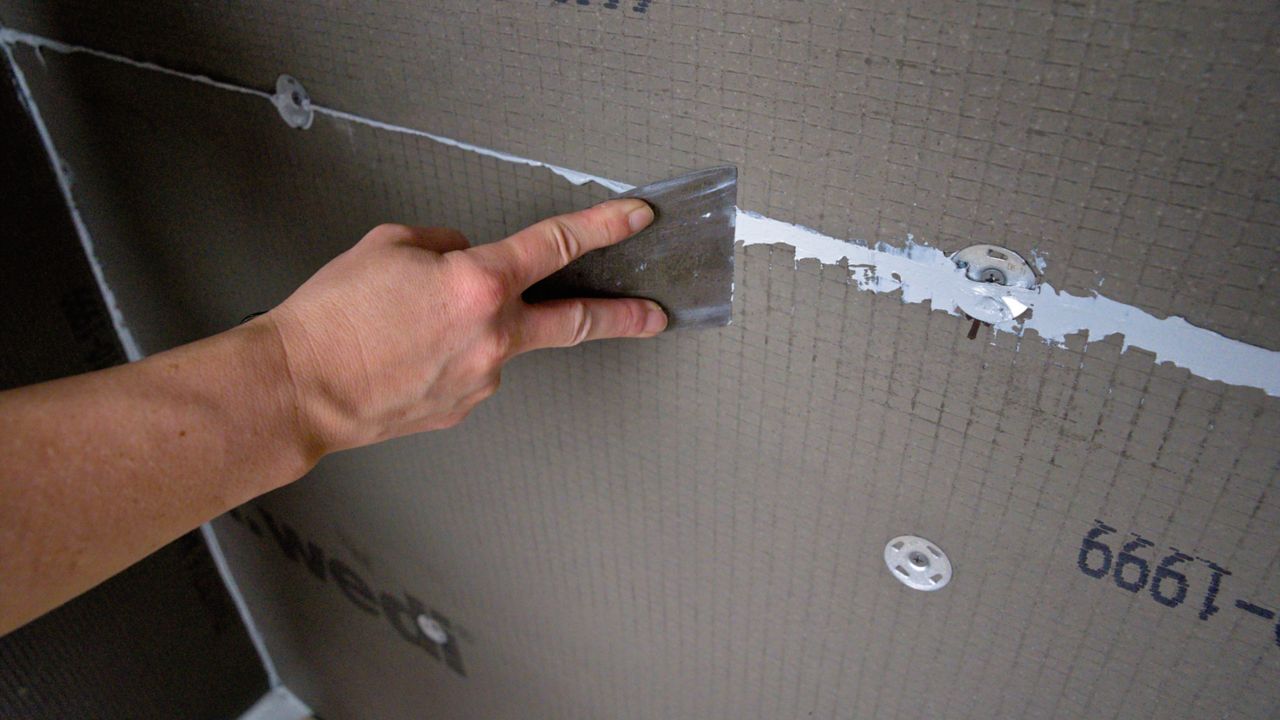 Spreading excess sealant with a putty knife at the seam where two shower backer boards meet.