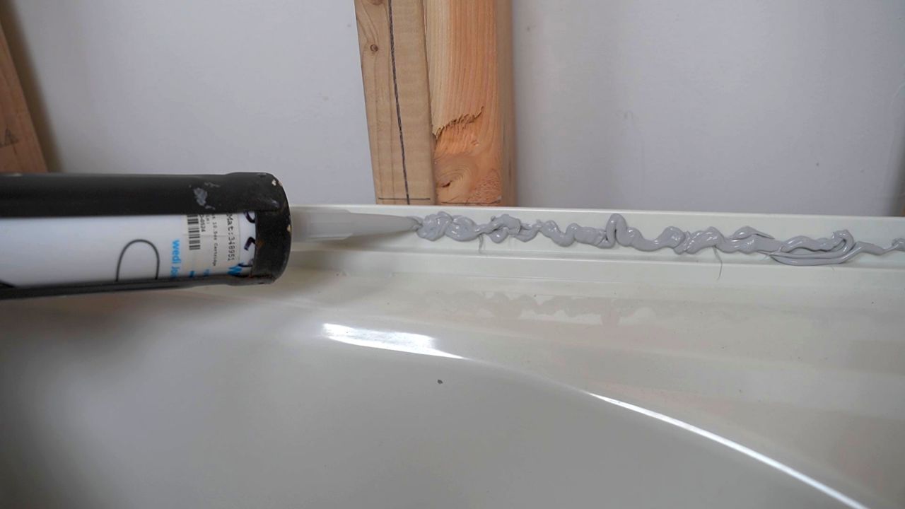 Adding waterproof sealant along the tub flange before hanging the first row of backer boards for shower walls.