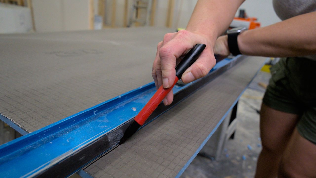 Using a straight edge to mark the measurements of a shower wall onto a building panel.