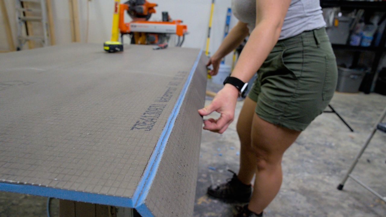 Using two hands to snap a shower wall building panel along a scored cut line.