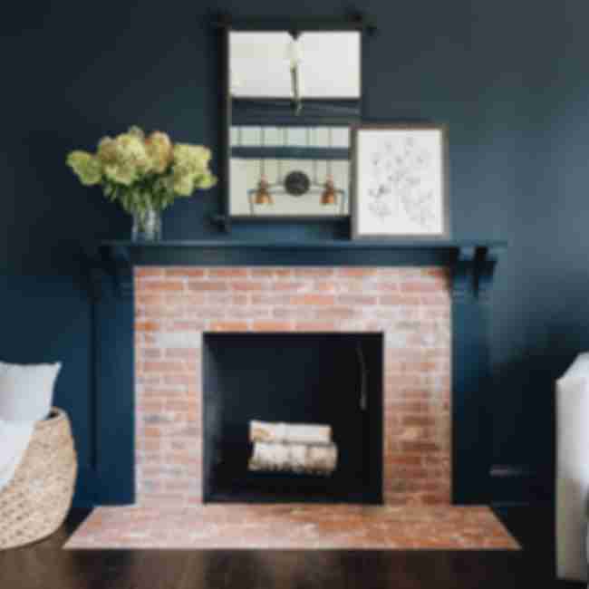 A transitional living room features dark wood floors and walls painted in a deep blue-green. This contrasts with the lighter brick-look subway tile used on the fireplace surround and hearth extension.