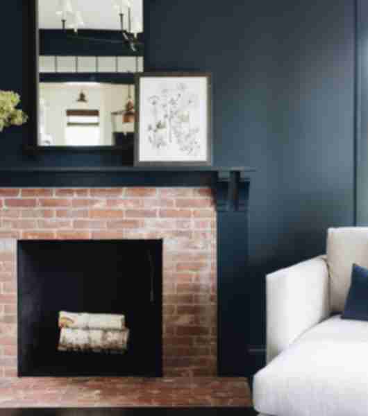 Fireplace surround with red brick tile. Black mantle and wall with pictures and a white chair.