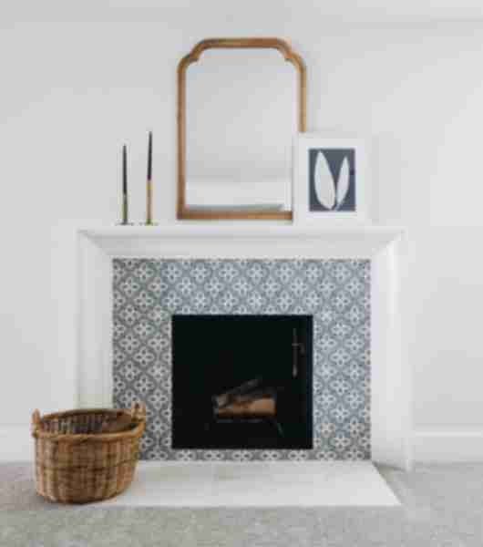 Set against a white wall and matching white fireplace mantel, this fireplace surround features blue and white tile in a geometric floral pattern.