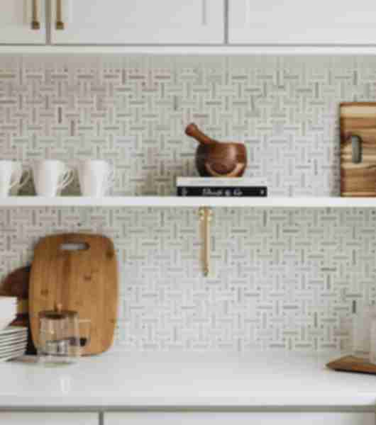 Kitchen counter and shelf with cups, cutting board and other cooking elements before white and beige tile