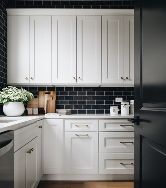 This kitchen features white upper and lower cabinets and a black travertine subway mosaic tile backsplash above the counter.