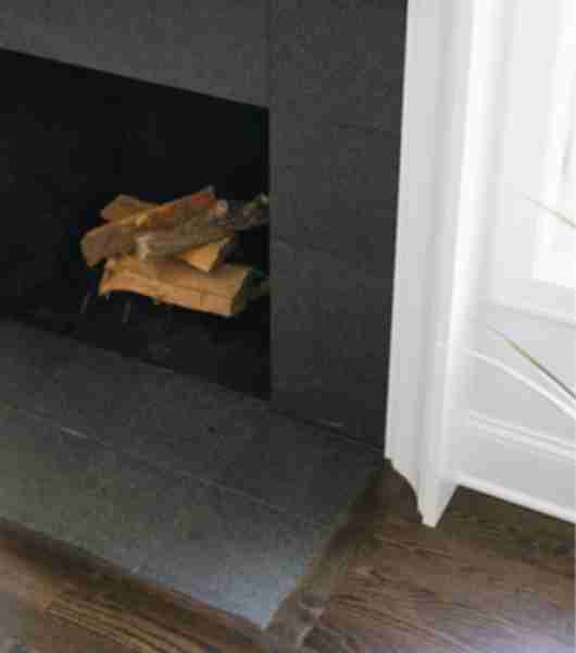The dark gray square granite floor tiles used for the hearth of this fireplace also surround the front face of the fireplace, adding understated drama to this living room.