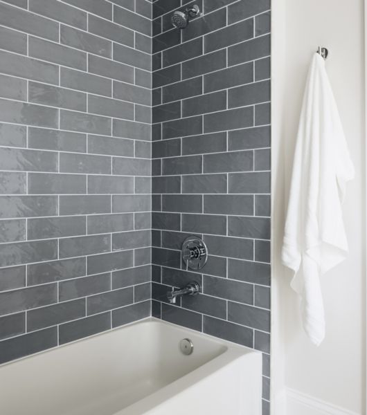 These shower walls feature 4x12-inch gray subway tiles arranged in a timeless brick-lay pattern. The tiles have slightly oversized proportions, with a wavy surface and high-gloss finish.