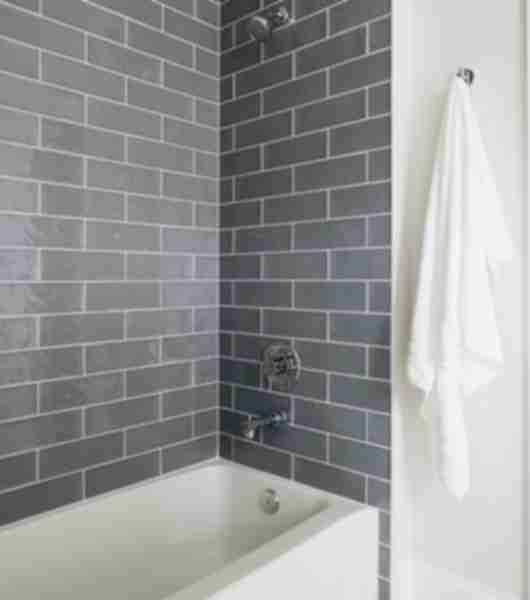 These shower walls feature 4x12-inch gray subway tiles arranged in a timeless brick-lay pattern. The tiles have slightly oversized proportions, with a wavy surface and high-gloss finish.