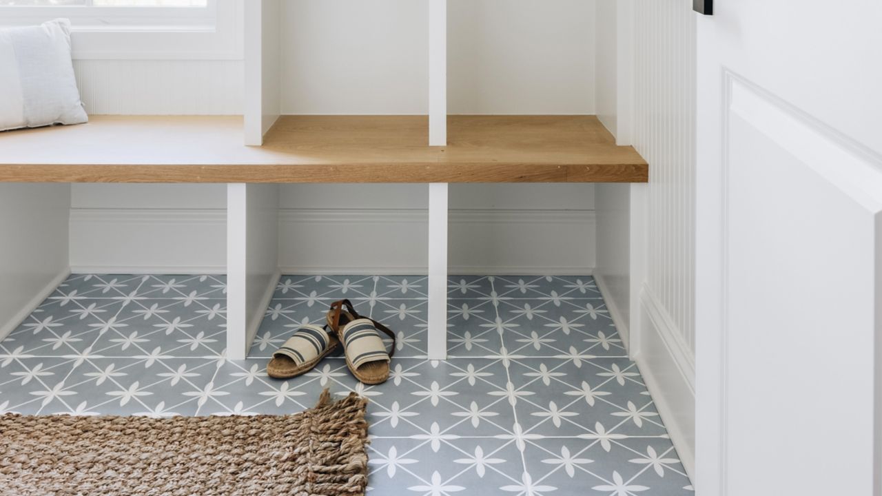 
A mudroom entryway features a white bench with a wood seat and built-in cubbies, sitting on a light blue and white starburst patterned tile floor.