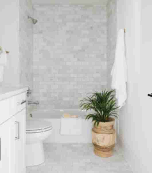 This three-piece bathroom includes a white vanity, white toilet and white tub. The three interior shower walls feature cool grey marble subway tile that extends from the tub all the way up to the ceiling.