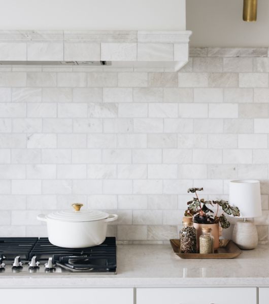 This beautiful kitchen features a light gray, polished marble subway tile backsplash. The subway tile extends up to the range hood over the stove, where it is then framed out with coordinating pieces of stone trim tile.