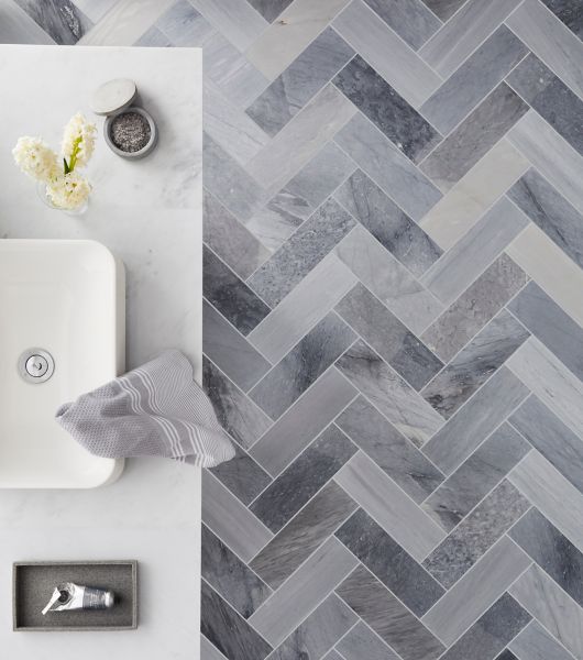 A bathroom floor with grey marble in a herringbone pattern. 