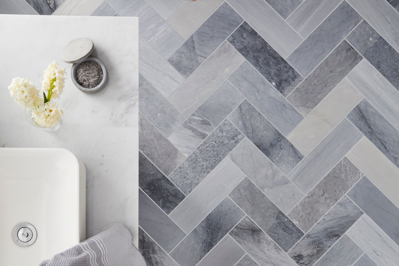 Bathroom floor tile laid in a herringbone with natural marble and a aerial view of a vessel sink.