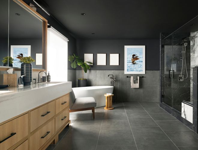 A modern bathroom with large-format grey floor and wall tile and a shower featuring black with white veined marble-look tile.