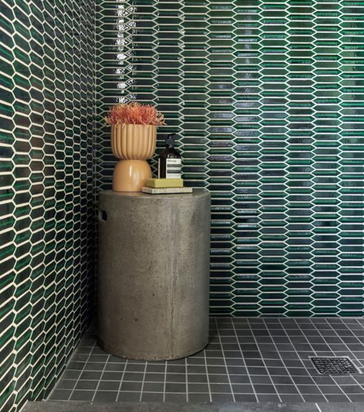 A large, open shower area with emerald green picket tile walls and a black square-shaped tile floor with a small round table.