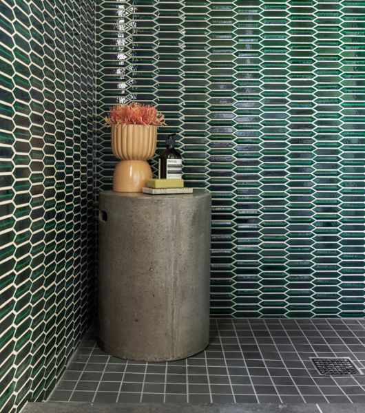 A large, open shower area with emerald green picket tile walls and a black square-shaped tile floor with a small round table.