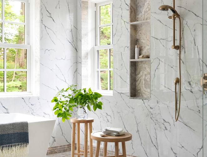 This spacious bathroom features white marble-look tile with dark grey veining and hexagon-shaped travertine tile floor.